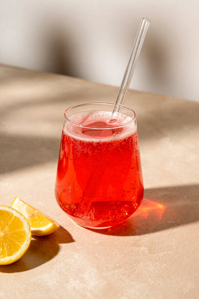 istock Red cocktail drink with fresh lemon, neutral background, sun light and shadows 1428641800