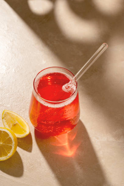 istock Red cocktail drink with fresh lemon, neutral background, sun light and shadows 1428641834