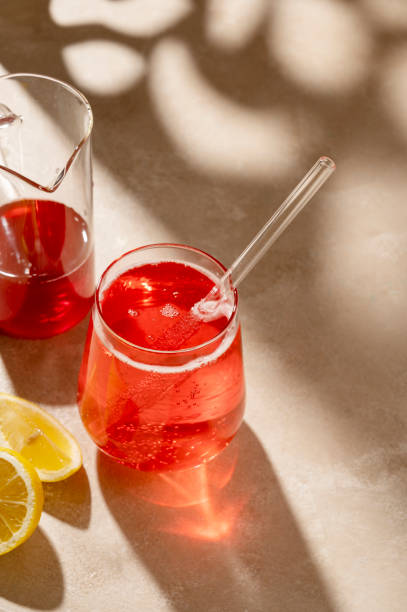 istock Red cocktail drink with fresh lemon, neutral background, sun light and shadows 1428641851