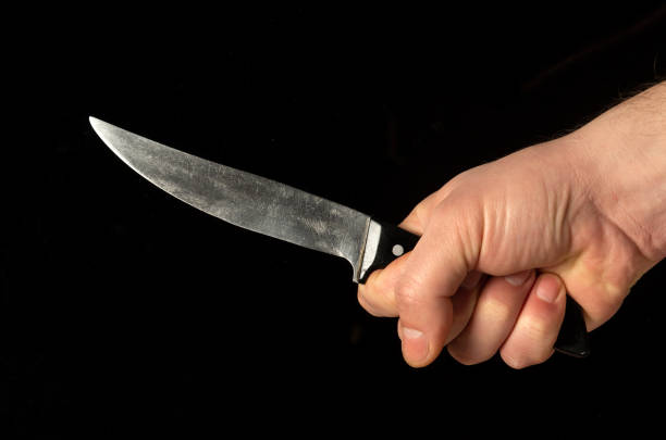 istock Men's hand holds sharp knife isolated against black background 1428644504