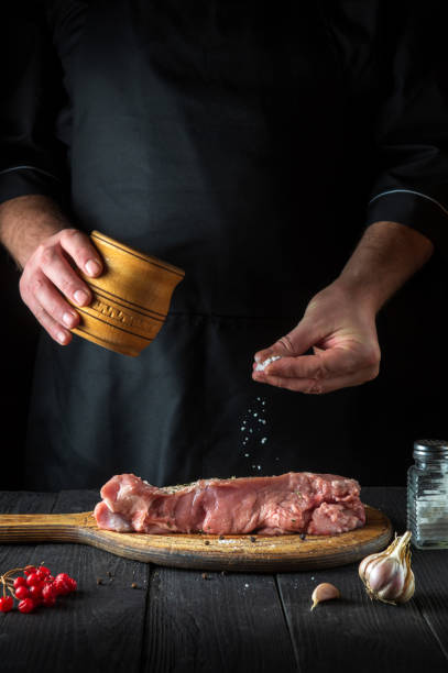 le chef prépare de la viande de veau crue. avant la cuisson, le chef ajoute du sel au bœuf. le plat national est préparé dans la cuisine du restaurant - veal calf meat baking photos et images de collection