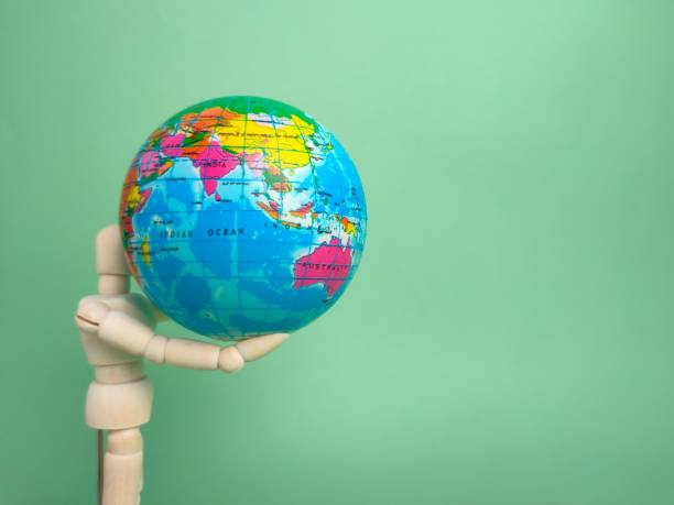 istock Wooden mannequin holding earth globe on a green background with copy space. 1428645330