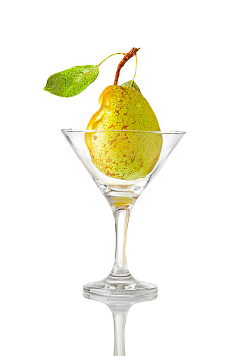 Ripe freshly picked pear with water drops on leaf in  transparent martini glass. Isolated on white background. Studio shot.