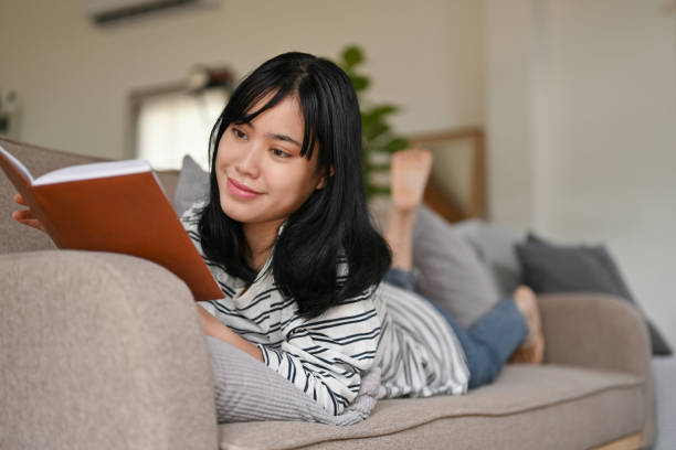 istock Charming and relaxed Asian female enjoys reading a book while lying on her comfortable sofa 1428651988