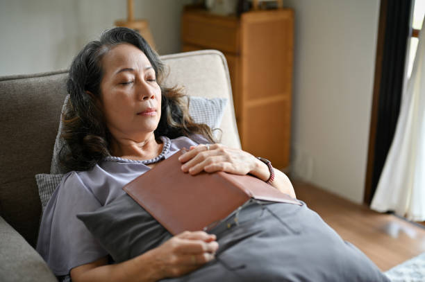 istock Calm Asian aged-woman sleeping on a couch in her living room, fall asleep while reading a book 1428652121