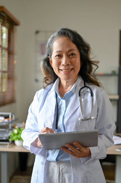 タブレットを持ったプロのアジア人先輩女性医師が医院に立っています。 - language therapy ストックフォトと画像