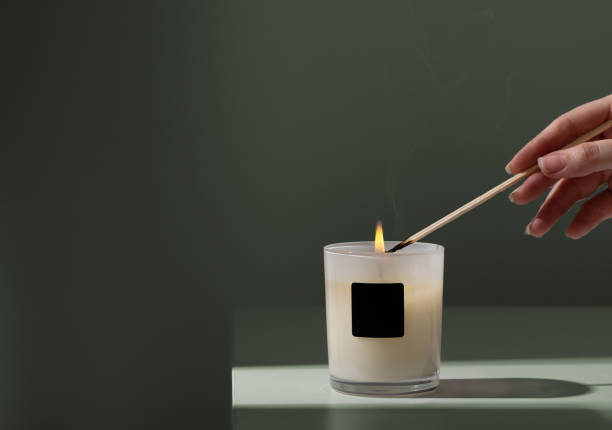 여자는 녹색 배경에 나무 막대기로 촛불을 켭니다. - aromatherapy candles 뉴스 사진 이미지