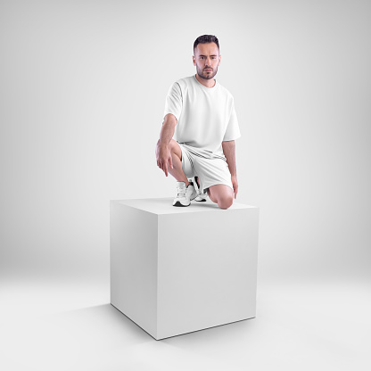 isolated mockup of trendy white men's oversized t-shirt with shorts on man sitting on cube. Clothing template for presentations of design, print, pattern.