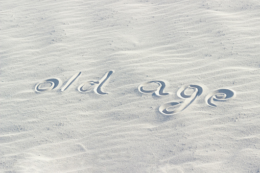 old age is written with a finger on the white sand. the concept of aging and age-related problems and diseases, word on the sand