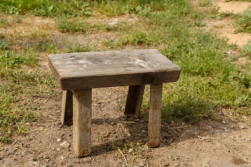 Old homemade wooden stool with metal legs. A small stool standing on the ground