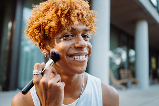 African american visagist holding brush and preparing makeup at the street while looking at the camera. Self identify concept