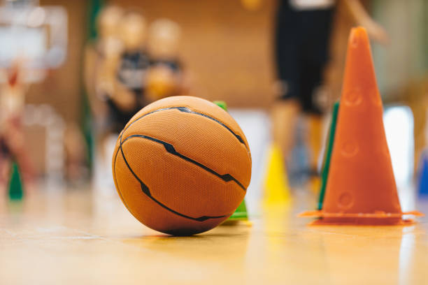 Basketball Training Game. Basketball Training Equipment on Sports Court Wooden Parquet - Basketball Floor. Close Up on Cones and Ball with Blurred Players and Coach Playing Basketball Practice Game Basketball Training Game. Basketball Training Equipment on Sports Court Wooden Parquet - Basketball Floor. Close Up on Cones and Ball with Blurred Players and Coach Playing Basketball Practice Game sports training drill stock pictures, royalty-free photos & images
