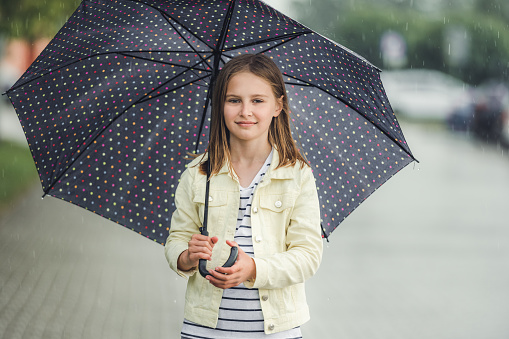 Pretty girl kid under umbrella in rainy day outdoors. Pretty preteen child walking in city in cloudy wet weather portrait