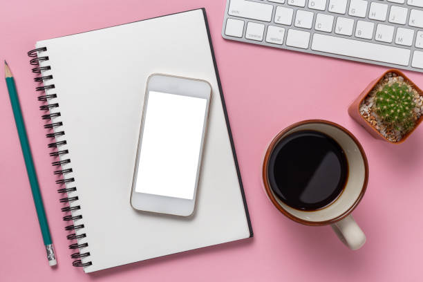 Top view office desk with empty smartphone, computer and office supplies on a pink background