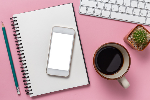 Top view office desk with empty smartphone, computer and office supplies on a pink background