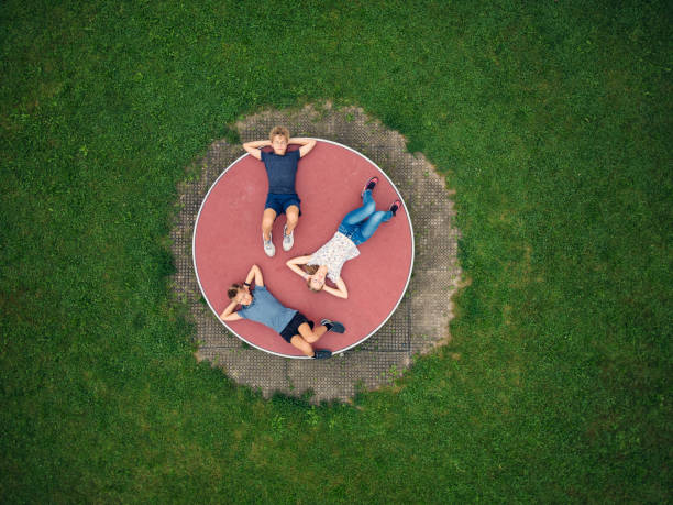 Three kids enjoying resting on playground wheel carousel Drone view of brothers and sister having fun lying on playground. Kids are lying on on a giant spinning wheel carousel on the playground.
Shot with DJI Mini Pro 3 slow motion photos stock pictures, royalty-free photos & images