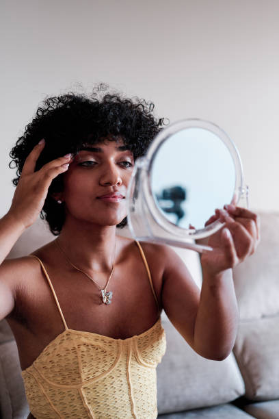 istock Confident transgender woman looking herself in a small mirror while sitting on a sofa at home. 1428669249