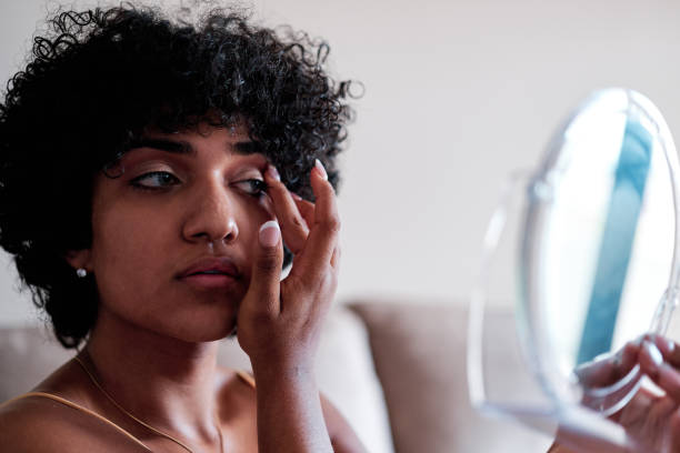 istock Transgender woman holding a small mirror while applying eyeshadow on eyes with fingers. 1428669251
