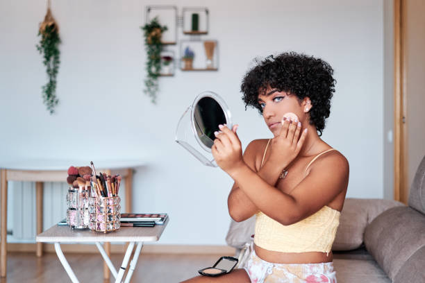 istock Transgender woman applying compact powder on her face while doing her makeup at home. 1428669313