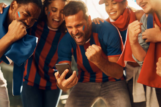 fãs de futebol animados comemorando o gol da vitória de seu time favorito enquanto assistiam a partida no smart phone. - soccer sport football fan - fotografias e filmes do acervo