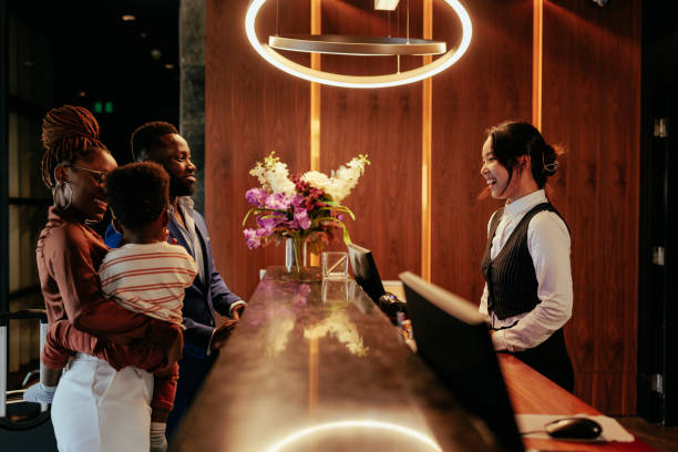 Busy front desk at hotel. A hotel clerk is welcoming guests that are checking in. It is a wealthy African American couple with their baby boy. The smiling clerk tends to them. hotel reception stock pictures, royalty-free photos & images