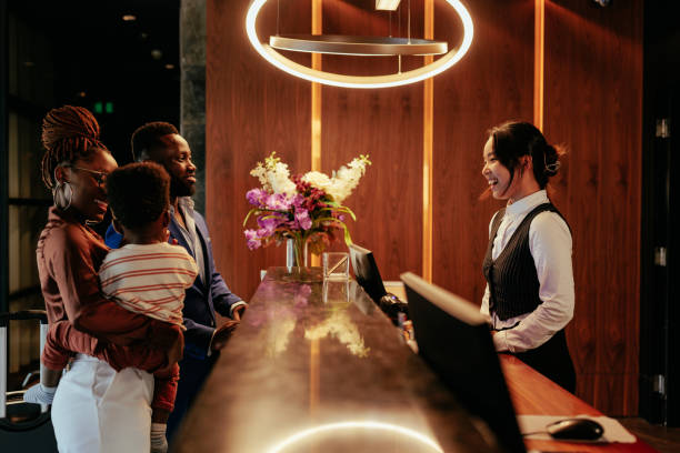 Busy front desk at hotel. A hotel clerk is welcoming guests that are checking in. It is a wealthy African American couple with their baby boy. The smiling clerk tends to them. concierge service stock pictures, royalty-free photos & images