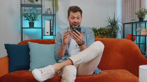istock Happy handsome man at home couch use smartphone typing browsing say wow yes found out great big win 1428676471