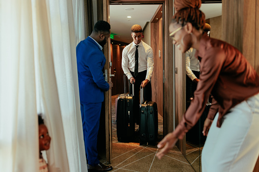 A wealthy family is in their hotel room. They open the door to let the hotel attendant with their luggage in.