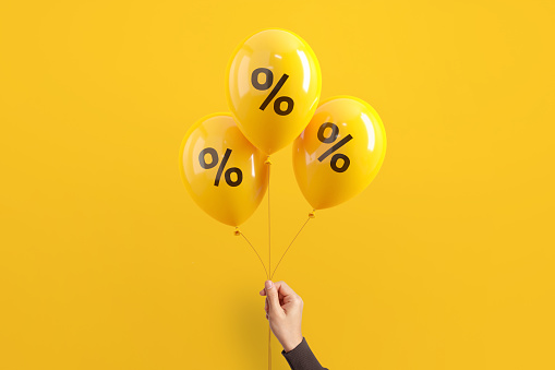 Hand of woman holding balloons with percent on yellow background, Minimal, Sale and discount.