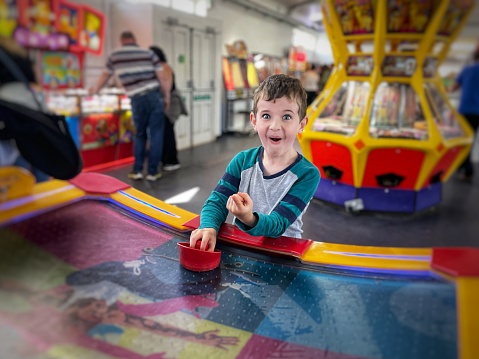 Young boy surprised by game of air hockey with his father at Paignton Pier, Devon, England