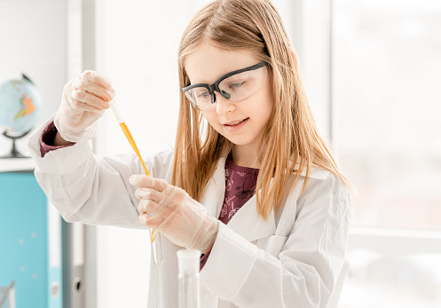 Girl doing scientific chemistry experiment wearing protection glasses and measuring liquid. Schoolgirl with test equipment on school lesson