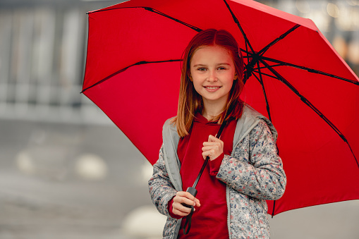 Preteen girl with umbrella standing under rain at autumn, looking at camera and smiling. Pretty kid portrait outdoors