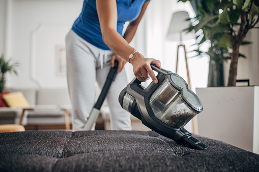 Woman housewife vacuuming furniture in a house with a hand-held portable vacuum cleaner