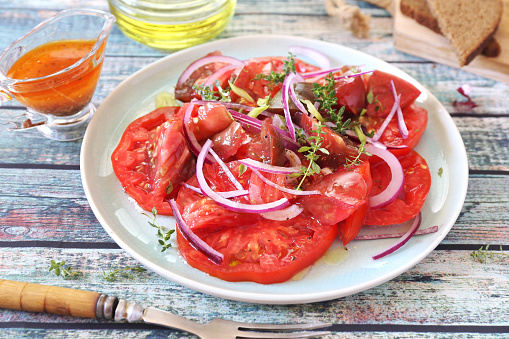 Tomato salad with red onion and spicy sauce of different varieties of tomatoes, two slices of rye bread on blue plate