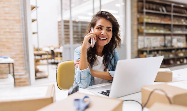 feliz jovem empresária falando ao telefone em um armazém - people women indoors retail - fotografias e filmes do acervo