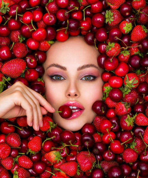 Attractive woman tasting cherry and strawberry. Beautiful woman with fashion makeup and a vivid background. Young girl with bright makeup and a berry background. Beautiful caucasian woman biting a berry. Attractive woman tasting cherry. Beautiful woman with fashion makeup and a vivid background. tasting cherry eating human face stock pictures, royalty-free photos & images