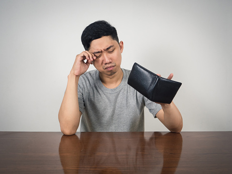 Young man crying about no money in his wallet on table
