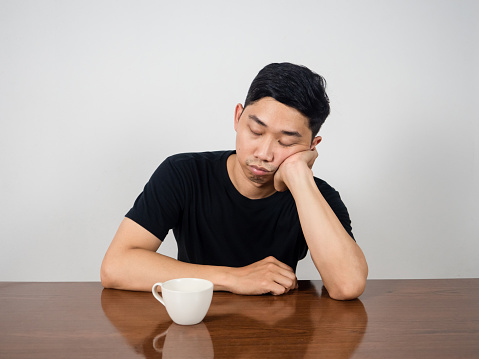 Sleepless man sitting sleep at table with coffee cup at morning