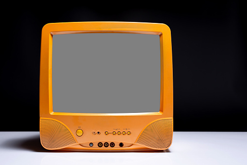 Old orange TV with cut out gray screen on white table with black background, retro, vintage television style