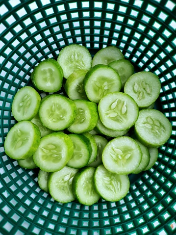 Sliced Cucumbers in dark green basket - food preparation.