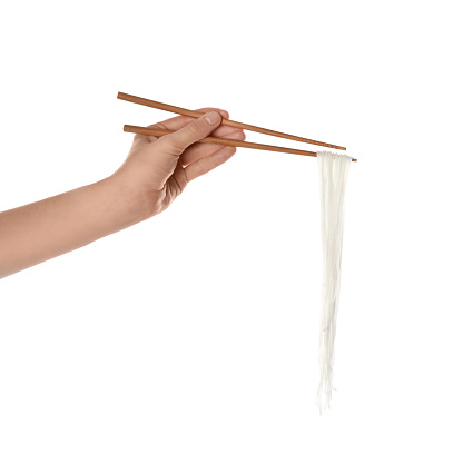 Woman holding cooked rice noodles with chopsticks on white background, closeup