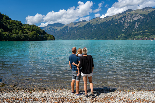 Mother, Father, & Daughter Enjoying the beautiful Swiss Alps towering over the turquoise clear water of Lake Brienz near Interlaken, Switzerland.