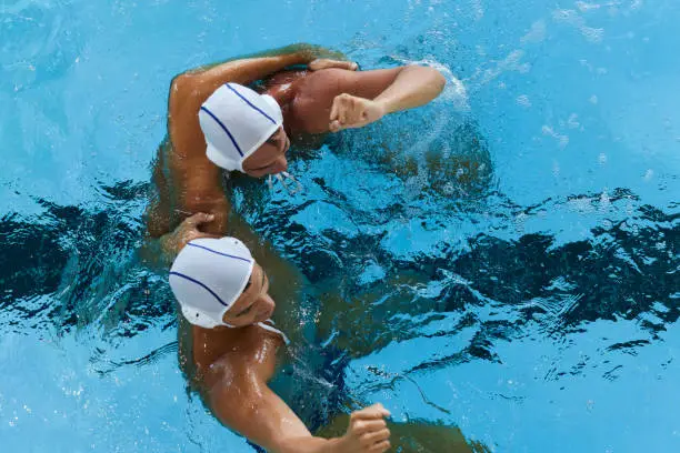 Two water polo teammates hug each other and celebrate a goal.