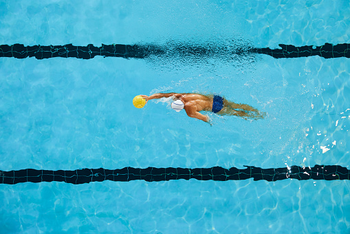 Mid race butterfly stroke swimming race in a olympic size swimingpool. Referee standing by the side.