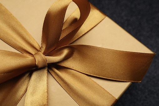 Caja de regalo dorada con lazo de satén sobre fondo negro. Closeup photo