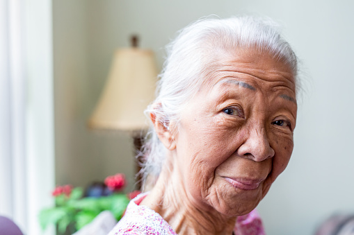 Portrait of a senior Filipino woman looking at the camera, in her living room
