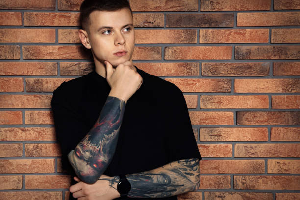 Young man with tattoos near brick wall
