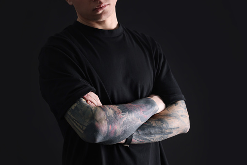 Young man with tattoos on black background, closeup