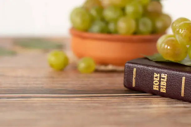 Closed Holy Bible Book with golden letters and a bunch of green grapes in a bowl on wooden background. Copy space. A closeup.