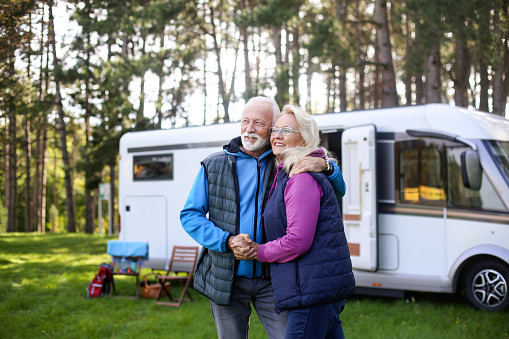 Senior couple camping in a forest with a recreational vehicle (motor home). Both about 65 years old, Caucasian people.